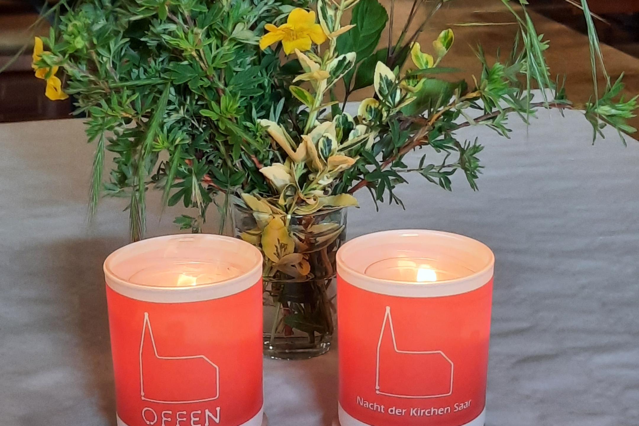 zwei Kerzen der Nacht der offenen Kirche brennen vor grünen Zweigen