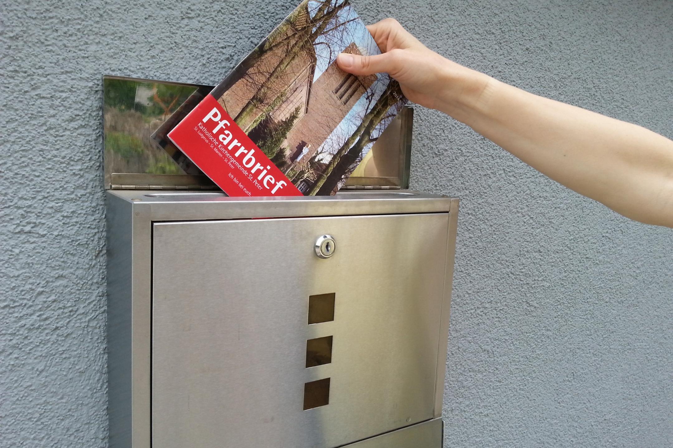 Ein Pfarrbrief wird in einen Briefkasten gesteckt.